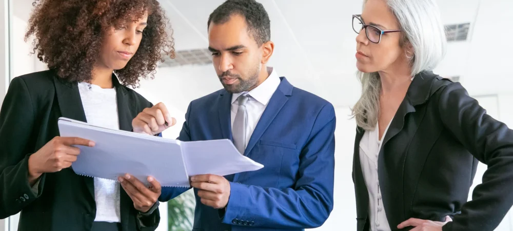 confident-office-employers-checking-documents-together-three-focused-professional-workers-holding-papers-signing-statistic-reports-meeting-room-teamwork-business-management-concept-compressed-1